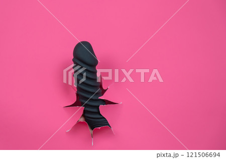 Black ribbed dildo sticking out of hole on pink background. Black ribbed dildo sticking out of hole on pink background. 121506694