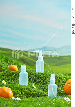 Cosmetic advertising template photo with nature scene on a green grass hill. Some unlabeled cosmetic bottles displayed in center, fresh fruits decorated around 121507435