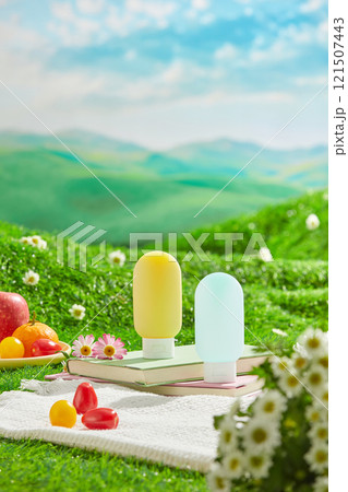 The advertising pic of picnic concept for sunscreen product, was shot from front view on green grass hill. Two unlabeled tube placed by side on book, next to a fruit dish and some decorative flowers 121507443