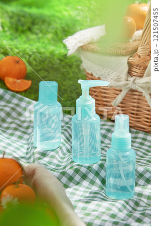 Overhead shot with a frontal view of a blue set product mockup placed on a green picnic mat, next to some tangerines and a basket. A concept for a picnic in the grass, perfect for cosmetics ad photos. Overhead shot with a frontal view of a blue set product mockup placed on a green picnic mat, next to some tangerines and a basket. A concept for a picnic in the grass, perfect for cosmetics ad photos. 121507455