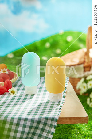 Frontal views of two bottle mockups are shown on a wooden table with a basket, tomatoes, and daisy flowers on a green picnic rug. A concept for a picnic in a lush meadow beneath a blue sky. Frontal views of two bottle mockups are shown on a wooden table with a basket, tomatoes, and daisy flowers on a green picnic rug. A concept for a picnic in a lush meadow beneath a blue sky. 121507456