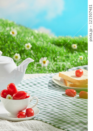 A green picnic mat with a variety of picnic items spread out on it, and empty space for displayed products. A picnic outside on a patch of green grass with daisy blooms, under a blue sky and sunshine. A green picnic mat with a variety of picnic items spread out on it, and empty space for displayed products. A picnic outside on a patch of green grass with daisy blooms, under a blue sky and sunshine. 121507481