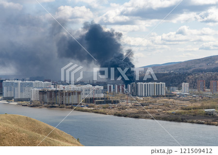 Black smoke from a fire in a city on the other side of the river. 121509412