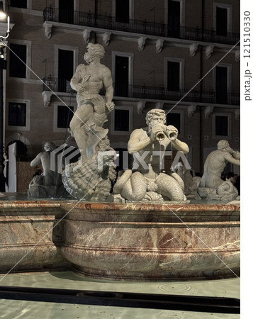 Elegant statues of mythological beings surrounded by water in a fountain create a captivating display at night in a charming historic square, enhancing the ambiance of the location. 121510330