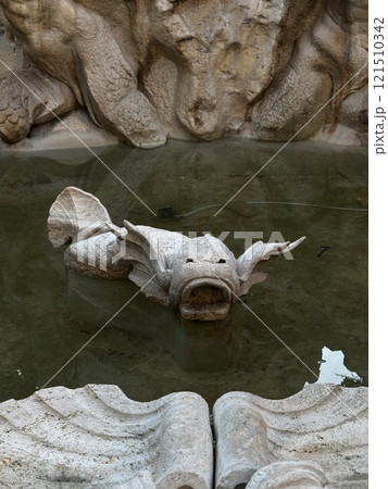 A weathered stone fish sculpture emerges from calm water, surrounded by intricate stone carvings in a historic courtyard, reflecting timeless craftsmanship and artistic beauty. 121510342