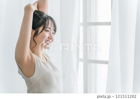 寝起き・起床時にカーテンの前で朝日を浴びる女性（脱毛・脇） 121511202