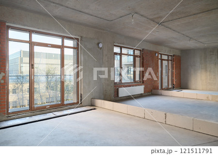 A Modern Unfinished Interior Space Featuring Large Windows Alongside Concrete Walls and Elements 121511791