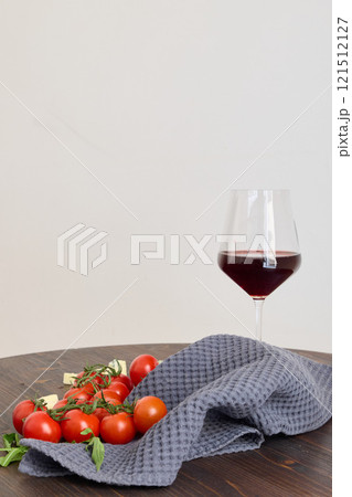 A Beautifully Arranged Red Wine Glass along with Fresh Cherry Tomatoes on a Dark Wooden Table 121512127