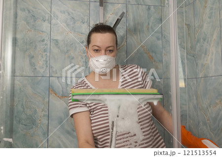 A Woman Diligently Cleaning the Shower with Soap and Wearing a Protective Mask for Hygiene A Woman Diligently Cleaning the Shower with Soap and Wearing a Protective Mask for Hygiene 121513554