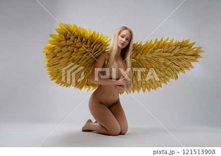 Model with golden feather wings poses gracefully in a minimalistic studio 121513908