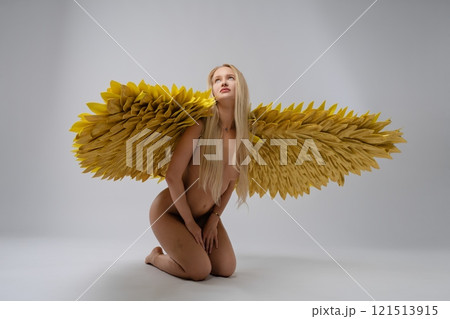 A model with golden wings poses elegantly in a minimalist studio 121513915