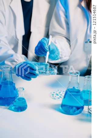 scientists in lab coats conducting research, handling glassware, and working with chemicals scientists in lab coats conducting research, handling glassware, and working with chemicals 121514687