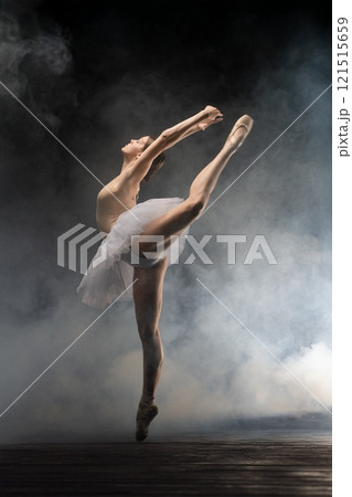 Graceful ballet dancer performing an elegant leap in a misty theater setting Graceful ballet dancer performing an elegant leap in a misty theater setting 121515659