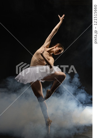 Dancer performing an elegant ballet pose amidst dramatic smoke effects 121515660
