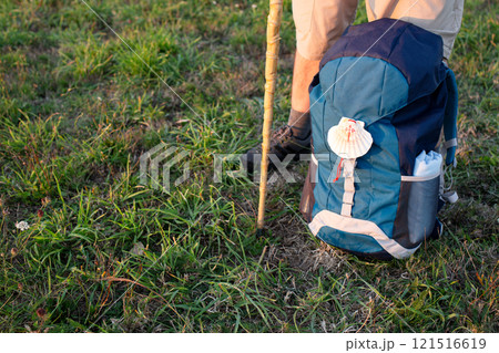 Pilgrim is taking a break during Camino de Santiago, resting his backpack with scallop shell on the grass. Copy space Pilgrim is taking a break during Camino de Santiago, resting his backpack with scallop shell on the grass. Copy space 121516619