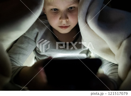 Child phone addiction. The boy at night, covered with a blanket, on the bed plays games on the smartphone and watches videos, cartoons 121517079