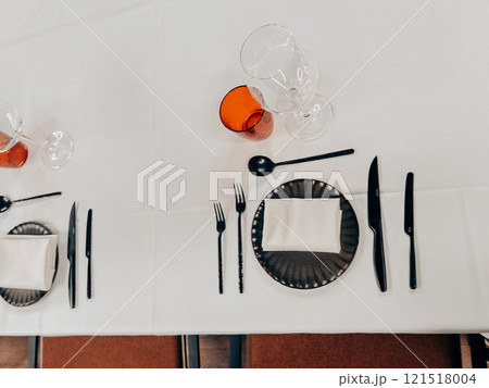 Table set in a restaurant. Glassware, red glasses on a white tablecloth on a table. Eating and drinking utensils. Forks and knives Plates with napkins Table set in a restaurant. Glassware, red glasses on a white tablecloth on a table. Eating and drinking utensils. Forks and knives Plates with napkins 121518004