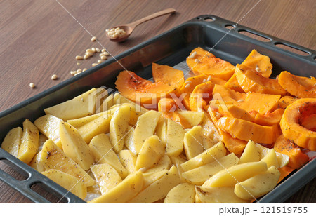 Sliced potatoes and pumpkin with pine nuts and spices on baking tray. Raw vegetables for baking. Healthy food in kitchen at home. Natural farm local products.  121519755