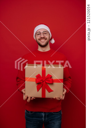 Happy man holding gift in his hands against red background with copy space 121520054