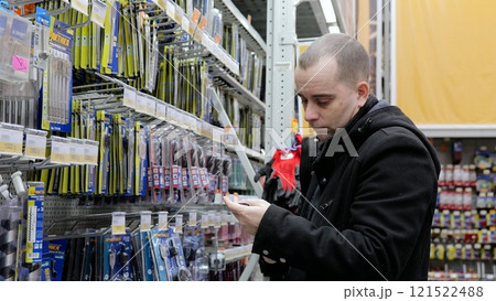 Focused male shopper selecting drill bit, comparing options while holding shopping list in hardware store aisle 121522488