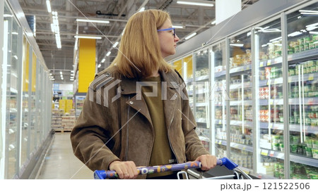 Young woman browsing dairy products and pushing a shopping cart in a contemporary grocery store 121522506