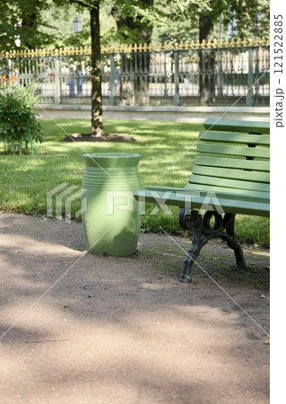 green dumpster, bench in a public place city street. plastic waste in trash can container. 121522885