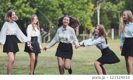 Five happy schoolgirls happily running and holding hands in the park to celebrate their first day of school 121524010