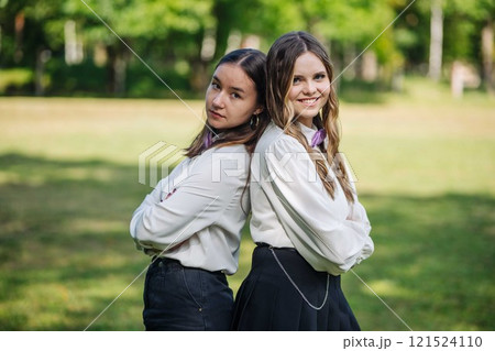 Two happy students with arms crossed, standing back to back in a park, smiling on their first school day Two happy students with arms crossed, standing back to back in a park, smiling on their first school day 121524110