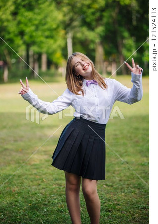 Girl in school uniform with bow tie making peace sign, winking and smiling on her first day of school 121524113