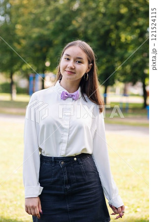 Photo of a happy young student girl with a purple bow tie, posing in a park on her first day of school 121524115