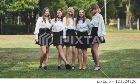Five high school students in white shirts and bow ties happily reunite for their first day back at school in a park 121524126