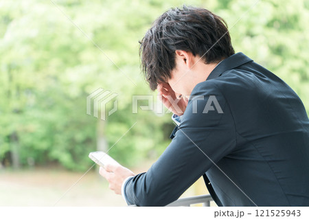 スマホを見ながら悩むビジネスマン（考える・退職・リストラ・パワハラ・プレッシャー・ストレス） 121525943