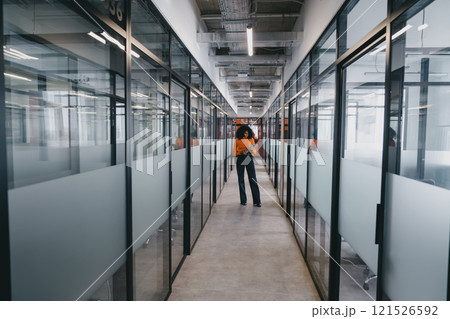 Confident Black businesswoman stands mid-corridor in an office, tablet in hand, showcasing leadership and modern business practices. Confident Black businesswoman stands mid-corridor in an office, tablet in hand, showcasing leadership and modern business practices. 121526592