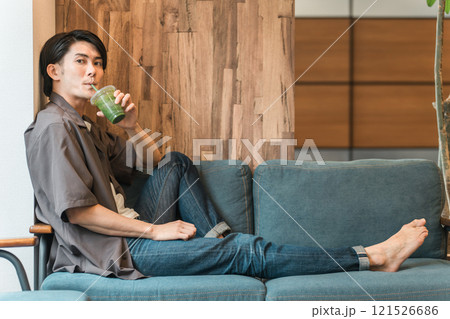 家のソファでグリーンスムージー・青汁・野菜ジュースを飲んでファスティング・断食・ダイエットする男性 121526686