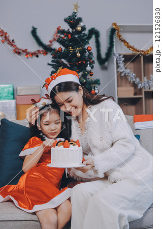 Merry Christmas and Happy Holidays. Cheerful mom and her cute daughter girl exchanging gifts. Parent and little child having fun near tree indoors. 121526830