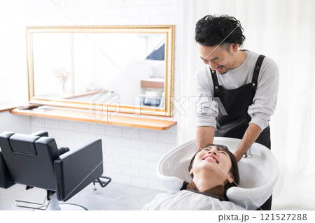 美容室のシャンプー台で髪を洗う男性美容師と洗ってもらう日本人女性客　女性は顔無し	 121527288