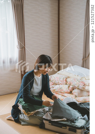 旅館でスーツケースに洋服を入れて帰り支度をする女性 121527382