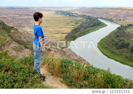 A hiking boy is looking at the river in a canyon from the hilltop. 121531152