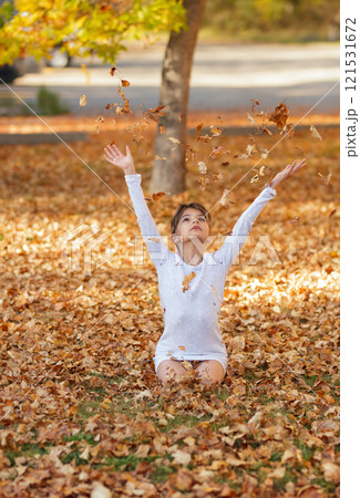 Girl is sitting on the ground in the fall park and throwing yellow leaves. Girl is sitting on the ground in the fall park and throwing yellow leaves. 121531672