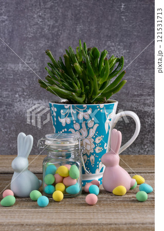 Cup with succulent, jar with Easter candies and bunny figurines. 121531713