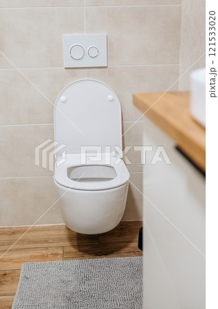 Toilet interior with wall hung toilet, white buttons and beige tiles 121533020