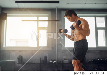 A man is exercising with dumbbells in a gym, focusing on improving his strength and health 121534181