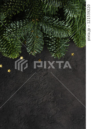 Close-up of fresh green pine branches with confetti in the shape of stars on dark textured background. A place for your text. Close-up of fresh green pine branches with confetti in the shape of stars on dark textured background. A place for your text. 121539220