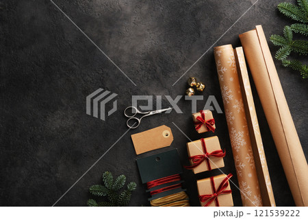 Gift wrapping items, kraft paper rolls, velvet ribbons, scissors and tags on dark background. Space for your text. Gift wrapping items, kraft paper rolls, velvet ribbons, scissors and tags on dark background. Space for your text. 121539222