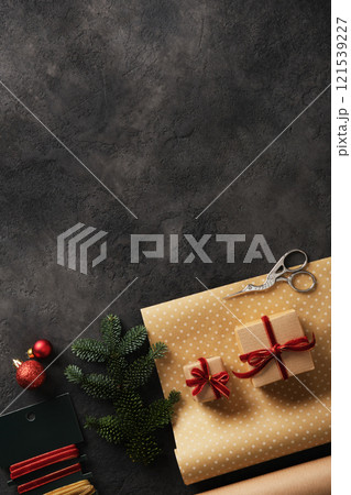 Supplies for wrapping gifts for Christmas and New Year's Eve. Kraft paper rolls, velvet ribbons, scissors, Christmas tree balls, spruce branch on dark background. Place for your text. Supplies for wrapping gifts for Christmas and New Year's Eve. Kraft paper rolls, velvet ribbons, scissors, Christmas tree balls, spruce branch on dark background. Place for your text. 121539227
