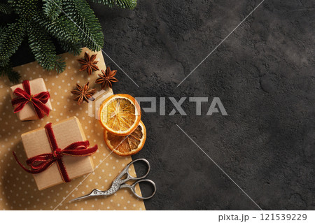 Banner with wrapping supplies for Christmas and new year gifts. Kraft paper, scissors, dried orange, anise stars, spruce branch on dark background. Place for your text. 121539229