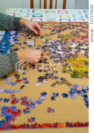 Female hands collect scattered puzzles on a brown background. Board games, hobby, leisure. Entertainment concept Female hands collect scattered puzzles on a brown background. Board games, hobby, leisure. Entertainment concept 121539288