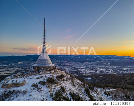 Snow blankets Jested Mountain as dawn breaks, casting a warm glow across the landscape. The iconic tower stands tall against the vibrant colors of the sky, creating a serene winter vista. Snow blankets Jested Mountain as dawn breaks, casting a warm glow across the landscape. The iconic tower stands tall against the vibrant colors of the sky, creating a serene winter vista. 121539397