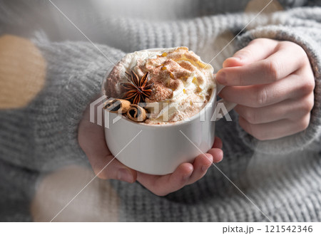Cup of hot chocolate with whipped cream, cinnamon and anise in hands against the background Cup of hot chocolate with whipped cream, cinnamon and anise in hands against the background 121542346