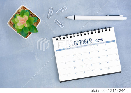 October desk calendar for 2025 year and plant pot with pen on blue cement. October desk calendar for 2025 year and plant pot with pen on blue cement. 121542404